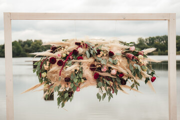 Wall Mural - Floral decoration hanging in wooden frame. Red, pink and white flowers. Lake water surface in background.