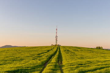 View of a broadcasting tower lying on a hill in the middle of a landscape in a field on a hill.