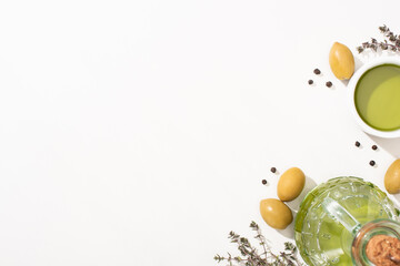 top view of olive oil in bowl and bottle near green olives, herb and black pepper on white background