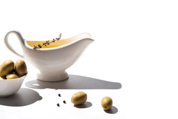 olive oil in sauce boat near green olives in bowl and black pepper on white background