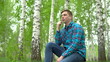 © Vital9c - A young man in nature is talking on the phone through headphones. A man sits on a stump in a birch forest with headphones.