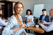 © Prostock-studio - Happy Businesswoman Looking At Camera Sitting With Colleagues In Office