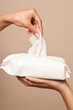 Hygiene. Female hands take wet wipes from white packaging on a beige background. Daily hygiene for the prevention of viral and bacterial infections.