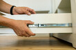 © bilanol - Close up of carpenter hands installing wooden drawer on sliding skids in contemporary cupboard cabinet.