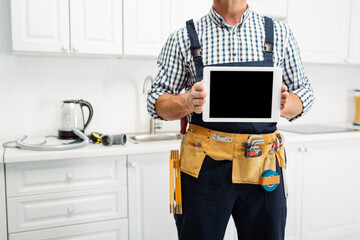 Wall Mural - Cropped view of plumber in tool belt holding digital tablet in kitchen