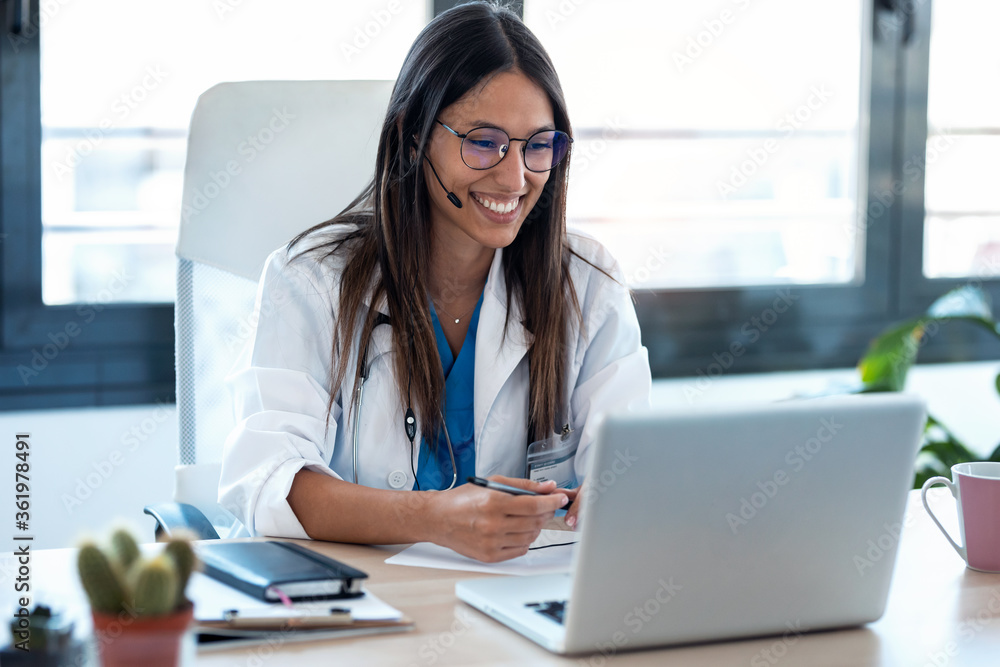 Female doctor talking with colleagues through a video call with a laptop in the consultation. - obrazy, fototapety, plakaty 
