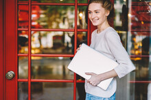 Cropped Image Of Positive Young Woman Dressed In Casual Outfit With Modern Laptop Computer In Hand Standing In Urban Settings Near Entrance Red Door In Stylish Coffee Shop.Promotional Background