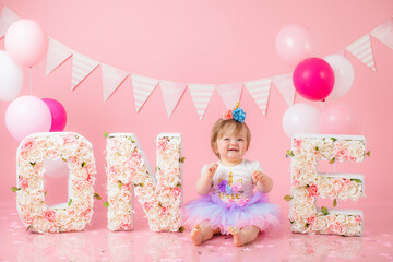 Smash cake party. Little cheerful birthday girl with first cake. Happy infant baby celebrating his first birthday. Decoration and photo zone for first year. One year baby celebration. Pink decor.