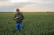 © Zoran Zeremski - Senior farmer standing in wheat field holding tablet and examining crop during the day.