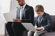 handsome businessman and his son in formal wear using laptops at home