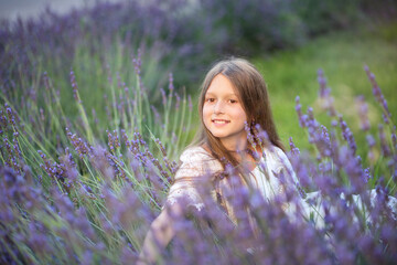 Wall Mural - Beautiful girl with long hair at sunset in the park. Girl in the lavender field. The child walks in nature. Summer sunsets
