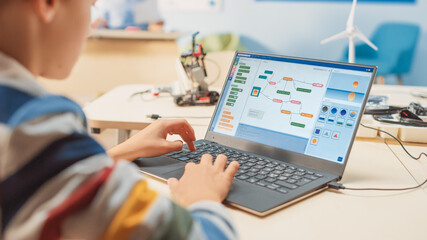 smart schoolboy uses laptop to program software for robotics engineering class. elementary school sc