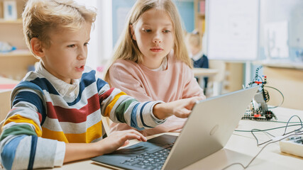 brilliant schoolgirl and schoolboy talk and use laptop to program software for robotics engineering 