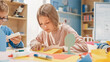 © Gorodenkoff - Elementary School Arts & Crafts Class: Cute Little Blond Girl Has Fun with Her Classmates on the Handicraft Project, Uses Colorful Paper to Fold Beautiful Origami