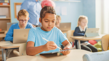 Wall Mural - Elementary School Computer Science Class: Cute Girl Uses Digital Tablet Computer, Her Classmates work with Laptops too. Children Getting Modern Education in STEM, Playing and Learning