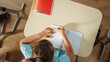 © Gorodenkoff - Top View Shot of Elementary School Classroom: Girl Sitting at the School Desk Working on Assignments in Exercise Notebooks.