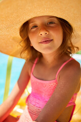 portrait of little girl in hat relaxing in swimming pool, swims on inflatable yellow mattress