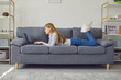 © Studio Romantic - Girl lying on her stomach on the couch uses lapot at home.