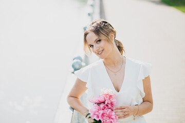 Young beautiful lady in white dress, with the bouquet of peonies.