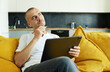 © oes - Young attractive smiling guy is browsing on his laptop, sitting at home on a cozy sofa at home, in casual outfit. Blogger freelancer