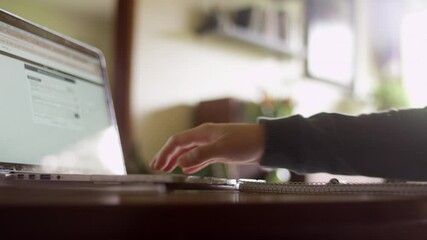 Pan across the hands of a person working on a laptop at home