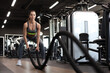 © ty - Fit woman using battle ropes during strength training at the gym.