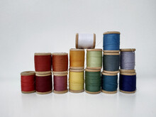 Colored Spools Of Sewing Thread On A White Background. Sewing Masks, Clothes, Multi Colored Rainbow Colored Threads. Small Spools Of Colored Thread Stand In Several Rows, A Wall Of Spools Of Thread