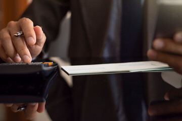 Wall Mural - Businessman hand holding mobile smart phone, write and signed blank  cheques with calculator on the desk at office. Paycheck concept.