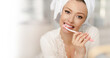 © ANR Production - A woman is brushing her teeth. Morning oral hygiene. Close-up with copy space. Attractive girl with a bath towel on her head after a morning shower