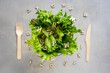 Frischer grüner Salat in einer weißen Schüssel mit Holz Buchstaben und Besteck auf einem grauen Hintergrund, Draufsicht, Humor