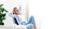 Leinwandbild Motiv Young woman relaxing under air conditioner at home. Girl resting on couch, enjoying cool fresh air in cozy living room. White background, copy space. Self isolation, social distance in quarantine.