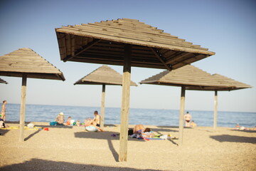 Wall Mural - Wooden beach canopies on a sea sandy beach. On a blurred background people sunbathe