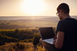 © Seleznov_Molchanova - man with laptop sitting on the edge of a mountain with stunning views of the valley