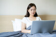 © DG PhotoStock - Upset Asian woman working on the bed by using laptop computer. A stress in freelance career during unstable economic. Unhappy and stressful Asian woman working in the bedroom.