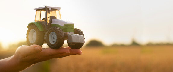 Autocollant - Woman farmer holds a toy tractor on a background of a wheat field. 