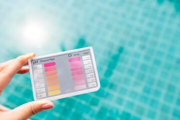 Wall Mural - Pool tester in girl hand over blurred blue water background, summer outdoor day light, swimming pool water tester tool