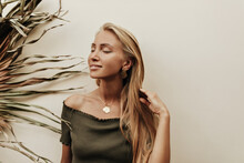 Charming Pretty Woman In Khaki Top Smiles With Closed Eyes. Blonde Young Lady In Dark Green T-shirt Poses Near Palm Leaf.