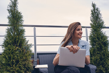 Cheerful young woman using laptop on rooftop terrace