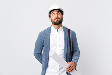 Young architect man with helmet and holding blueprints isolated on white background and looking up