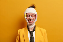 Health Care And Injury Concept. Happy Positive Young Man Smiles Broadly And Shows Missing Teeth, Recovers After Being Beaten, Wears Bandage On Head And Formal Suit, Has Funny Face Expression