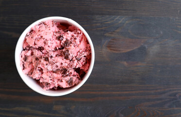 Wall Mural - Cup of delectable creamy strawberry chocolate chunk ice cream on dark brown wooden background	