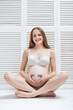 © somemeans - Beautiful young pregnant woman sitting on floor in Lotus position and smiling. Vertical frame