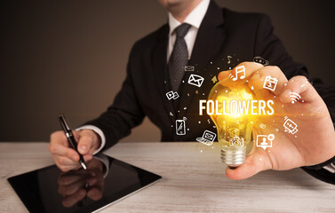 Businessman holding light bulb with FOLLOWERS inscription, social media concept