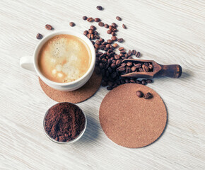 Delicious fresh coffee. Coffee cup, coffee beans, beer coaster and ground powder on light wooden background. Flat lay.