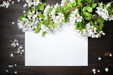 Photo of blank paper poster and spring flowers on wooden background. Responsive design mockup. Flat lay.