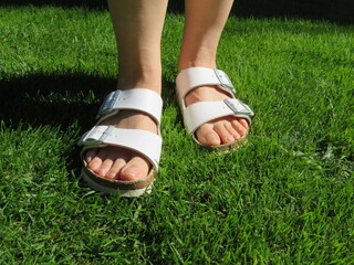 Closeup photo of  woman feet wearing  scandals standing on grass during summer