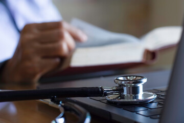 Female doctor reading text boo with  medical stethoscope on the desk in room at clinic. Medical knowledge and education concept.