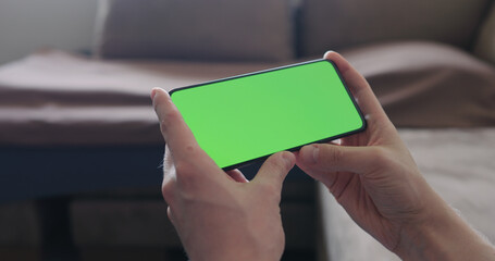 Poster - Closeup young man sit on a couch and watch something on a smartphone with green screen