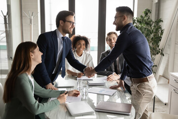 Wall Mural - Smiling multiethnic male business partners shake hands close deal make agreement at team meeting in boardroom, excited diverse businessmen handshake get acquainted greeting at briefing in office