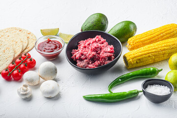 Wall Mural - Raw ingredients for tacos with minced beef meat, corn tortillas, chili, avocado, over white background. Side view.